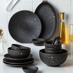 black dinnerware set with gold speckles on the plates and cups, next to wine bottle