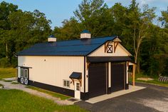 a large white barn with a black roof and two garage doors on the side of it