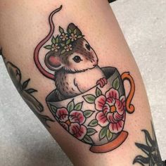 a mouse in a teacup with flowers on it's head is sitting on the leg