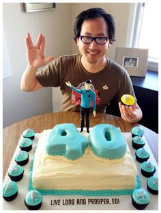 a man sitting at a table with a cake and cupcakes in front of him