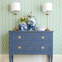 a blue dresser with two lamps on top and a vase sitting on it's side