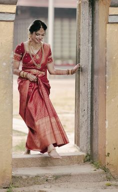 a woman in a red and gold sari walking out of a doorway with her hand on the door handle