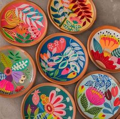 six colorful painted plates sitting on top of a cement floor with leaves and flowers in them