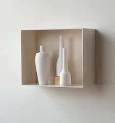 three white vases are sitting in a box on the wall next to each other