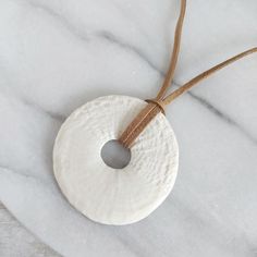 a white round ornament hanging on a brown string with a leather cord around it