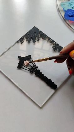 a person is painting an image on a glass plate with paintbrushes and glue