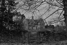 black and white photograph of an old house in the woods with stone walls around it