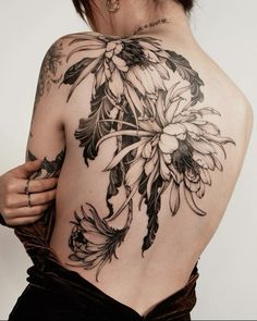 the back of a woman's body with tattoos on it and flowers in bloom