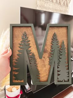 a person holding up a wooden letter that has trees on it and the letter m is made out of wood