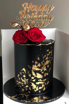 a black and gold birthday cake with red roses on top, sitting in a white box