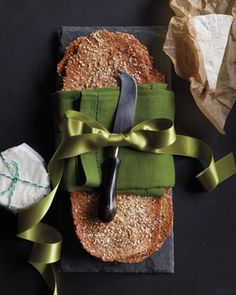 a piece of bread wrapped in green ribbon next to a knife and napkin on a black surface