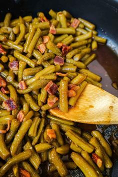 green beans and bacon are being cooked in a skillet with a wooden spatula