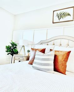 a white bed topped with lots of pillows next to a green plant in a bedroom