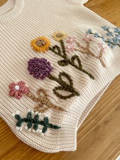 a knitted sweater with flowers and the word love on it is sitting on a wooden floor