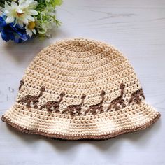 a crocheted hat with giraffes on it and flowers in the background