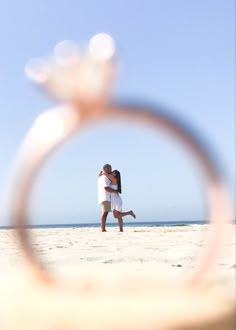 a man and woman kissing on the beach through a magnifying lens with an ocean in the background