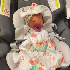 a baby doll in a car seat with its mouth open and tongue out, wrapped in a blanket