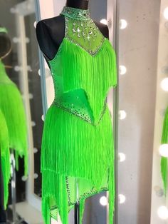 a green dress with fringes and beads on display in front of a lighted mirror