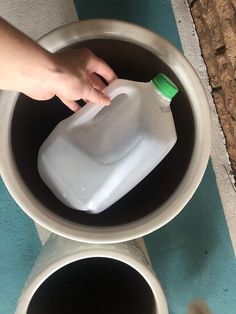 a person is holding a plastic bottle over two large pots with one being filled with water