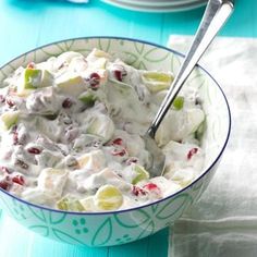 a bowl filled with fruit salad on top of a blue and white table cloth next to silverware