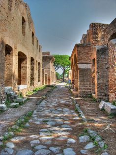 an old cobblestone street with people walking on it and trees in the background