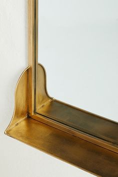 a gold framed mirror hanging on the side of a white wall with a shelf below it