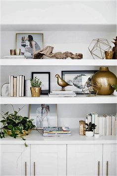 white shelves with gold vases, books and pictures on them in a living room