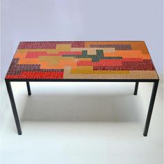 a table made out of mosaic tiles with black metal legs and an orange, green, yellow, red, and pink design