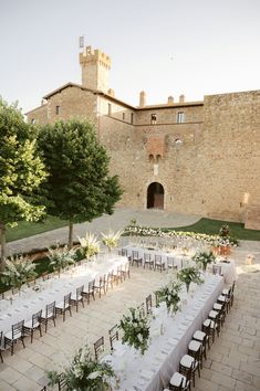 a long table with white linens and greenery is set up in front of an old brick building