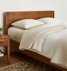 a wooden bed with white sheets and pillows