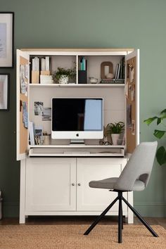 a desk with a computer on it and a chair next to it in front of a green wall