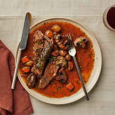 a white plate topped with meat and veggies next to a cup of wine