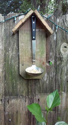 a bird house with a spoon hanging from it's side on a wooden fence