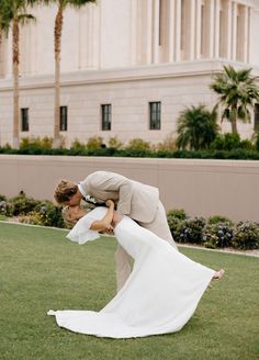 a bride and groom kissing in front of a building with palm trees on the lawn