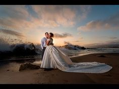 a bride and groom standing on the beach in front of an ocean wave at sunset