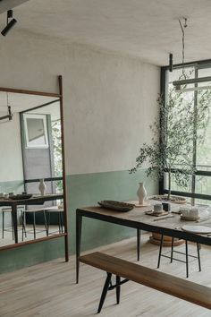 a dining room table and bench in front of large windows with mirrors on the wall