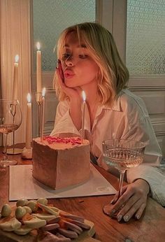 a woman sitting at a table in front of a cake with lit candles on it