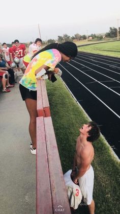 a man kneeling down next to a bench on top of a race track with other people watching