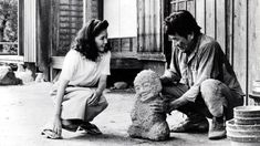 an old black and white photo of two people playing with a teddy bear in front of a house