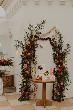 a table topped with a cake covered in flowers and greenery next to a wall