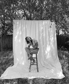 a man sitting on top of a stool in front of a white backdrop with trees