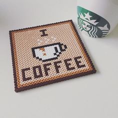 a cross stitch coffee coaster next to a cup of coffee