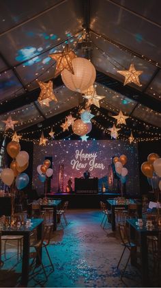 Festive New Year's party setup with hanging star lanterns, balloons, and a "Happy New Year" sign on stage.