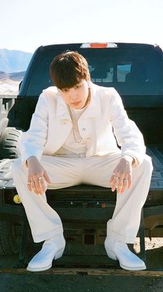 a man sitting on the back of a truck wearing white pants and a jacket with his hands in his pockets