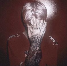 a young man with tattoos covering his face and hands in front of him, wearing a red shirt