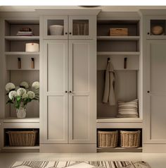 an organized mud room with white cabinets and wicker baskets on the floor, along with flowers in vases