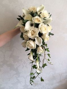 a bridal bouquet with white roses and greenery is held by a woman's hand