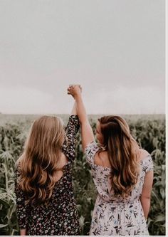 two women standing next to each other holding hands in front of a field of flowers