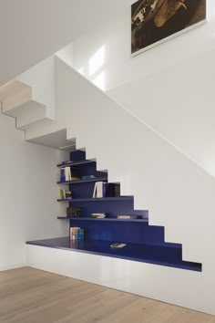 a blue book shelf under a staircase in a white room with hardwood floors and walls