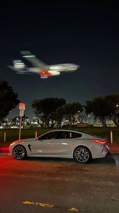 an airplane flying over a car parked in a parking lot at night with red lights